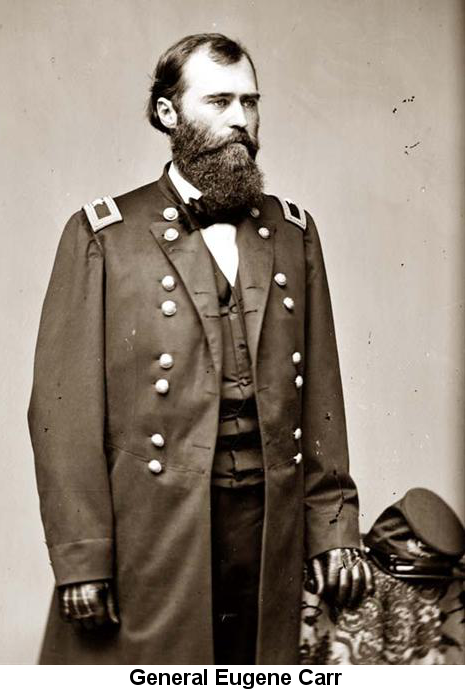 Black and white photograph of Union General Eugene Carr, standing, wearing an unbuttoned uniform overcoat and leather gloves, standing with his left hand on a draped table on which sits a Union forage cap
